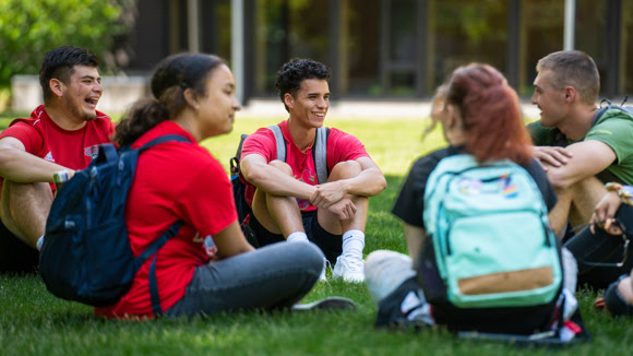 unnamed (8) Group of students with backpacks sitting in a circle on grass